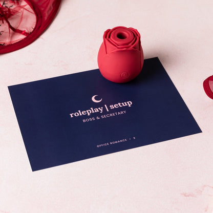 Rose suction vibrator on top of a gameplay card from the Office Romance set with red floral lingerie on the edges of the frame.