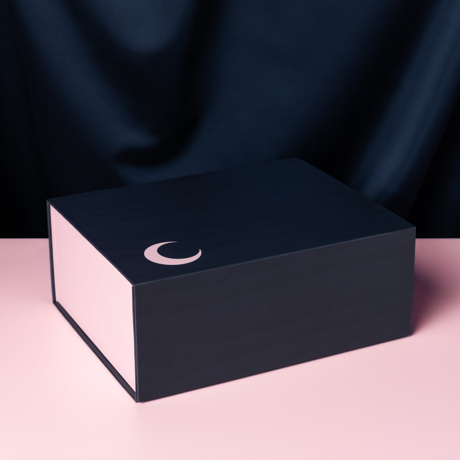 Closed Saturday Box on pink surface with blue, draped background