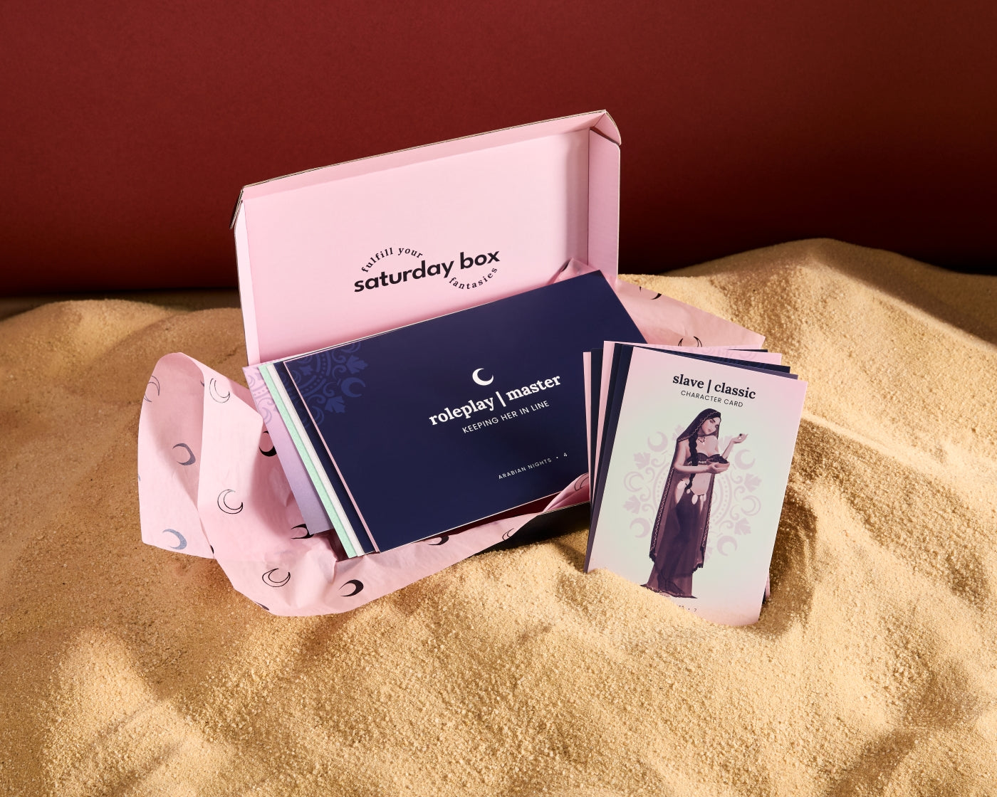 Pink role-playing game box with cards on a sandy surface