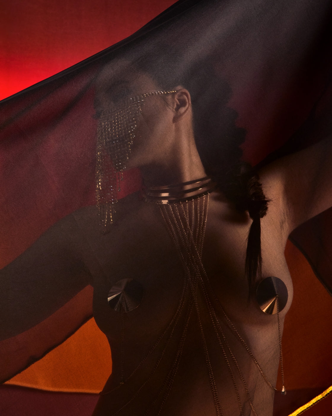 Woman covered by a sheer black veil trimmed with gold thread on a red background