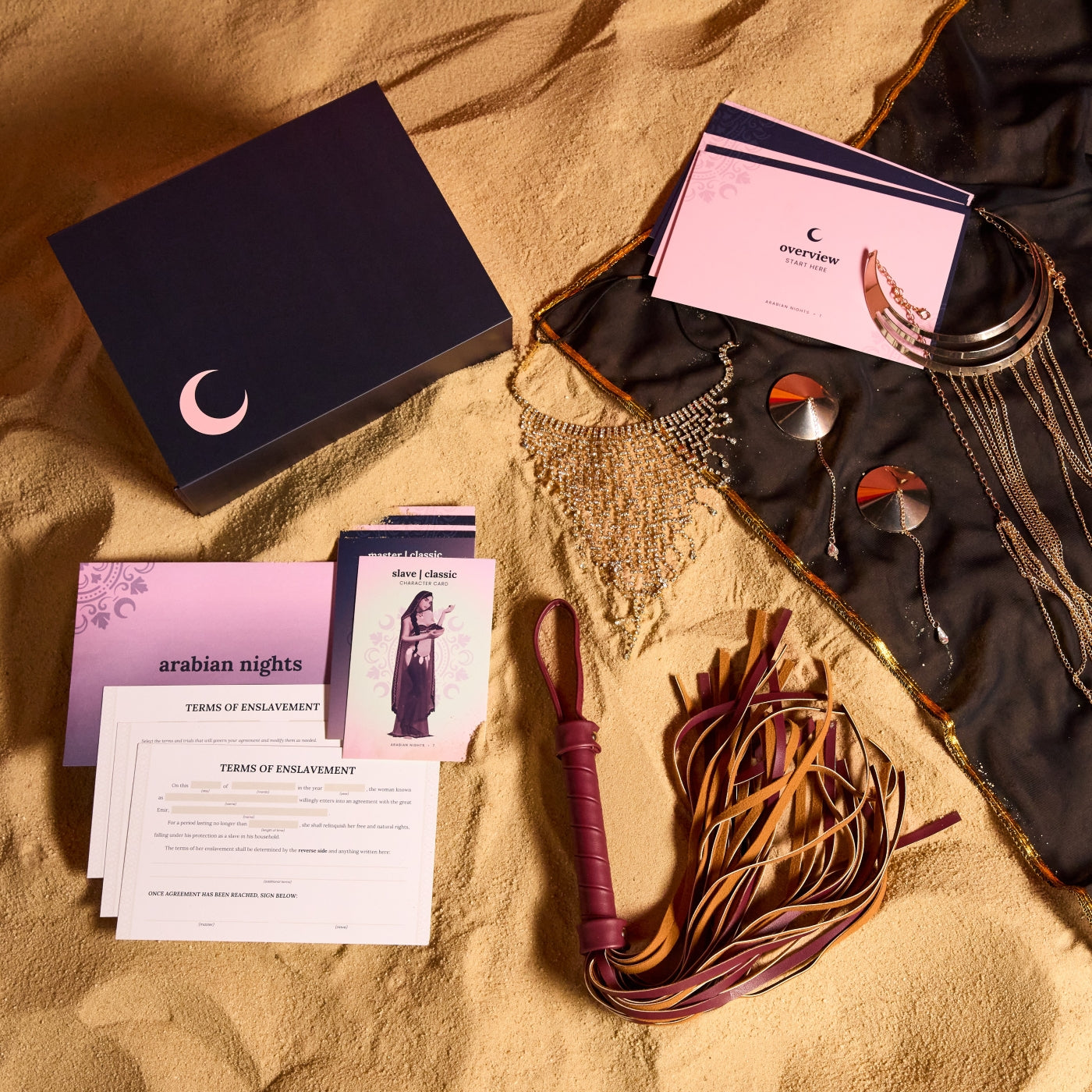 Collection of items including a box, cards, and accessories on a sandy surface.