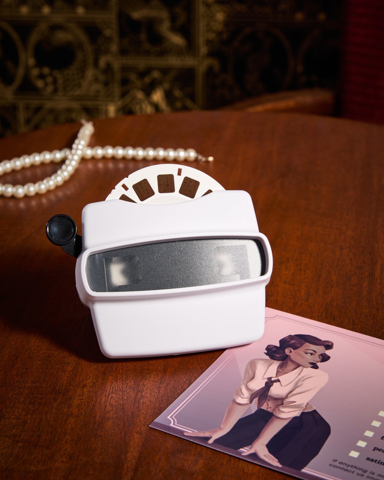 A viewfinder set on a wooden table with the product checklist in the foreground and a string of pearls in the background