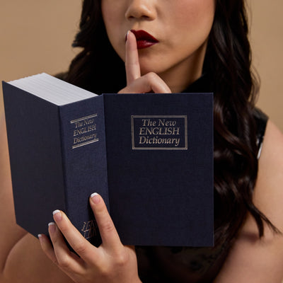 A person holding a blue hardcover dictionary to their face, making a shush sign with their finger