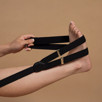 A pair of black loose lips suspenders being stretched by a foot.