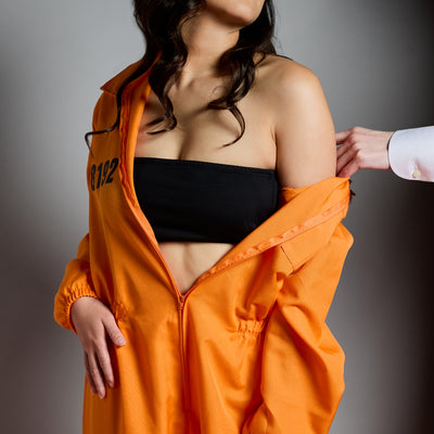 Woman wearing orange jumpsuit that's off the shoulder on grey background