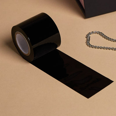 A roll of black self-adhesive tape laid out on a beige surface, with a small piece unrolled 