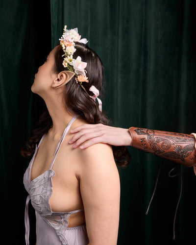 Woman in flower crown turned away from man with vambraces on green background