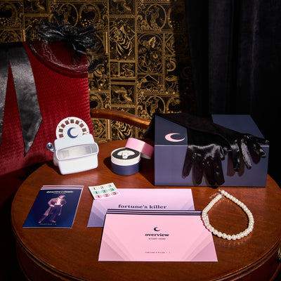 Contents of the fortune's Killer Saturday Box displayed on wooden table with a black and gold wallpaper and a black curtain behind them